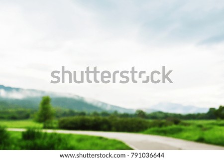 Blurry grass nature field with car road way in weather rainy cloudy day vintage picture style countryside of Thailand.