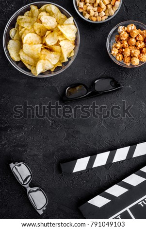 Crisp, popcorn, rusks for watching film. Clapperboard and glasses on black background top view copyspace