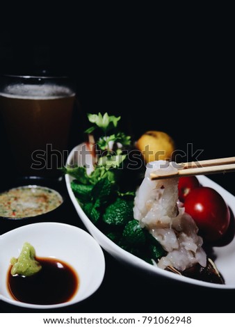Picture of Lobster sashimi, soy sauce, wasabi, Thai spicy sauce and a glass of beer on black background. Selective focus