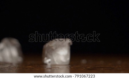 Ice cube bouncing and crashing on blue sheet with dark background table top in slow motion. Falling ice cubes on a black background