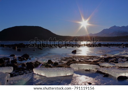 Spectacular Alaska scene featuring a sun burst, ice blocks on the shore, mountains and the ocean