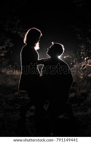 Young pair enjoying outdoors in the forest during night time and looking at each other.  Silhouette picture of the couple at the forest with backlight.