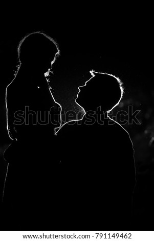 Young pair enjoying outdoors in the forest during night time and looking at each other.  Silhouette picture of the couple at the forest with backlight.