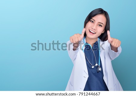 Happy asian woman doctor giving thumbs up over blue background