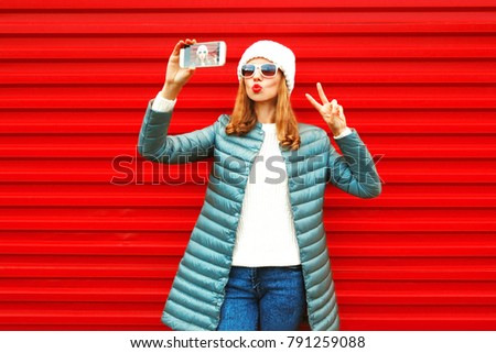 Fashion pretty woman takes a picture selfie portrait on a smartphone on red background
