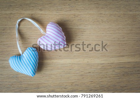 Close up and top view of two, pink and blue, striped, fabric, textile hearts that are bound together on wooden background, vintage toned. Love, romance or Valentine's day concept