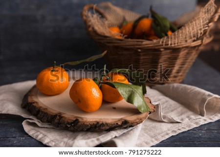 Kitchen table with cotton serviette and basket full of mandarins with leaves. Dark background