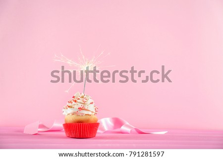 Birthday cupcake with sparkler on table against color background