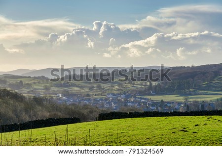 A green field with a village beyond and gowing cumulous clouds ont eh horizon, Cumbria, northern England