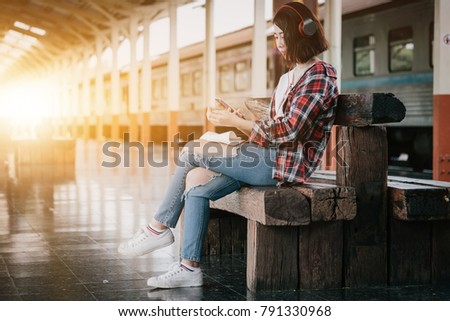 Hipster Backpacker at the train station with a traveler while using smart phone for travel plan and listen music. Travel concept.