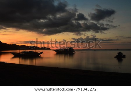 Beautiful gold and red sunset over calm sea without a wave and with two boats and black clouds