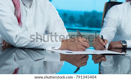 Two Saudi Businessmen Hands Signing a document, contract or making a deal Royalty-Free Stock Photo #791345404