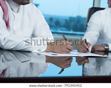 Two Saudi Businessmen Hands Signing a document, contract or making a deal