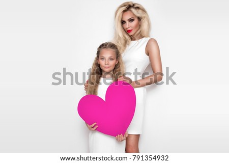 Beautiful blonde woman mother and daughter standing on a white background and holding a red heart