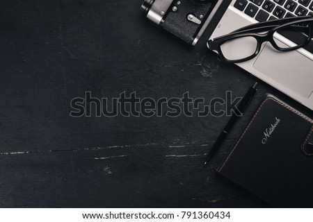 Office desktop. Laptop, camera, calculator, glasses, ruler, pen, pencil. On the black wooden surface. Top view. Free space for text.
