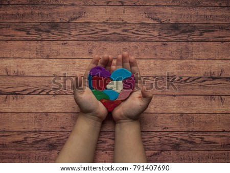 Child's hands holding a multicolored heart on wooden background with text space. World autism awareness day.