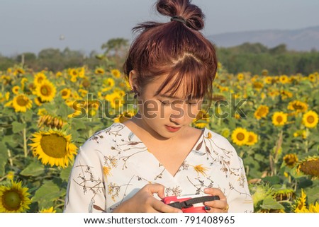 Asian girl pay attention on her smartphone during traveling in a sunflower farm at the Sunrise time.