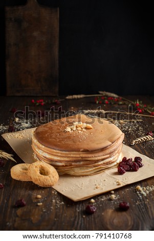 a pile of pancakes, berries, biscuits, a cutting board on parchment on a dark wooden table