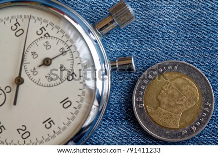 Thai coin with a denomination of ten baht (back side) and stopwatch on blue jeans backdrop - business background
