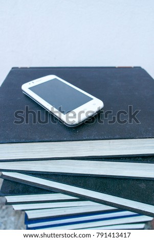 A mobile phone on a pile of books. 
