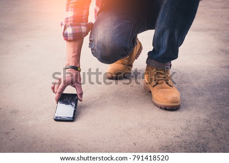 the abstract image of the man picking a broken smartphone up from sement floor. the concept of broken, accident, daily life, mobile phone, electronic, repairing, warranty and technology.