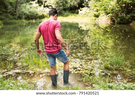 Teenage boy in rubber boots standing in lake.
