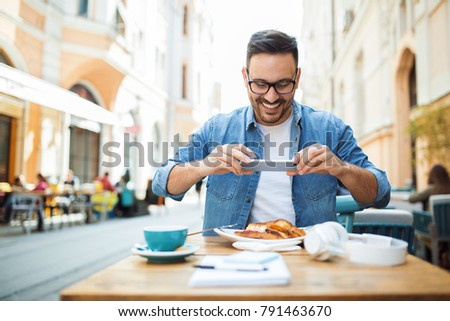 Smiling modern young man taking photo of his meal at the restaurant