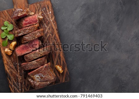 Closeup ready to eat steak new York beef breeds of black Angus with herbs, garlic and butter on a wooden Board. The finished dish for dinner on a dark stone background. Top view with copy space Royalty-Free Stock Photo #791469403