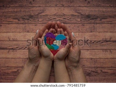 Autism awareness concept with heart of colorful pieces. Woman's and child's hands holding a multicolored heart.