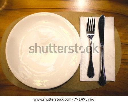 A white plate with silver fork and knife for eating pizza. That are on the wooden table.