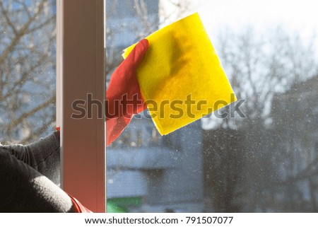 Photo of a female hand in a rubber glove cleaning a dirty window with a special rag