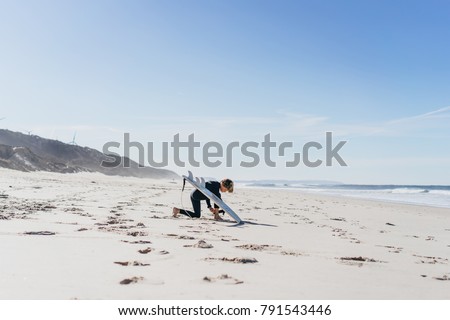 the boy kneads on the beach before surfing and runs into the water with a surf board.
Children and surfing concept, surfing in a wet suit.