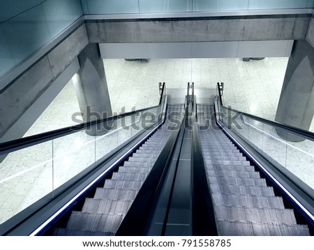 Looking down at an Escalator with no people. Escalator going down to another floor in a metro station. Clean and sleek modern interior design at a transportation hub. Monochromatic Photo filter added.