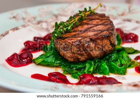 Grilled beef steak minion with with spinach and cherry sauce on a patterned plate. Side view