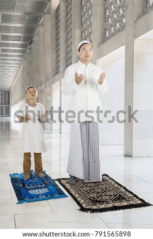 Picture of Muslim man with his son wearing Islamic clothes while praying to GOD in the mosque