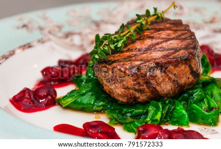Filet mignon. Grilled beef steak minion with with spinach and cherry sauce on a patterned plate. Side view