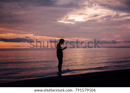Young man playing smarth phone on a beach by the sea watching the sunset