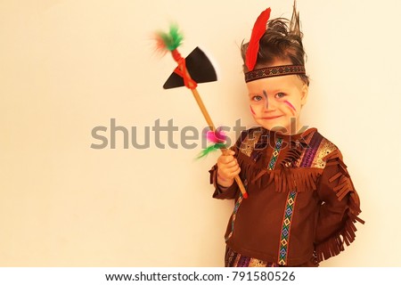 Cute smiling little boy in an Indian costume posing against the wall, a hatchet in his hand, hair is disheveled. Ready for Purim party