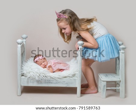 Little girl sits next her newborn sister