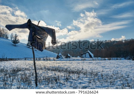 Sweater hanging in the rack to scare the birds coming to eat the wheat seedlings from the ground. In the background snow covered hills.