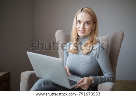 young smiling beautiful caucasian woman enjoys a laptop while sitting in a chair