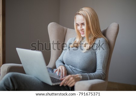 young smiling beautiful caucasian woman enjoys a laptop while sitting in a chair