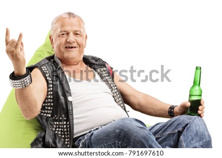 Old punker with a beer bottle seated on a beanbag making a rock hand gesture isolated on white background