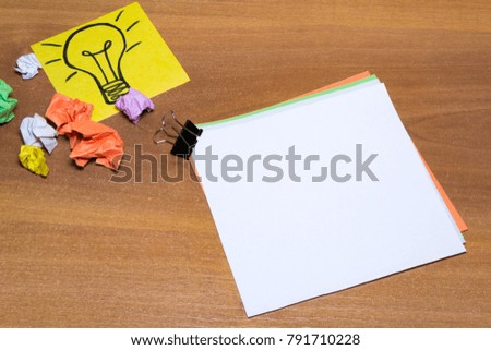 Idea concept with crumpled paper lightbulb and colored spiral notepad with pen on wooden desktop.
