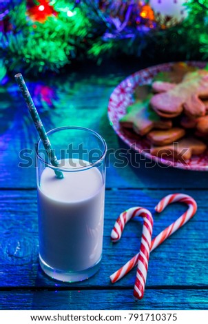 Picture of Christmas cookies, glass of milk, caramel sticks, spruce branches with burning garland