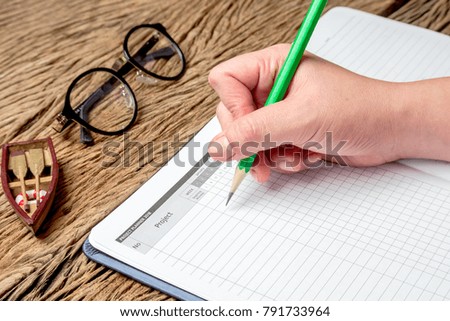 Businesswoman are writing annual business planning on diary book on the wooden table with pencils, crayons, mini both and glasses for annual business planning.