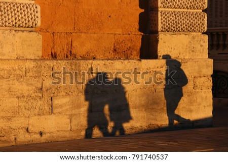 Abstract picture and pattern of shadows of people who are walking on the street in Montpellier France. Their human forms can be seen on the textured surface of an old stone wall lighted by the sun. 