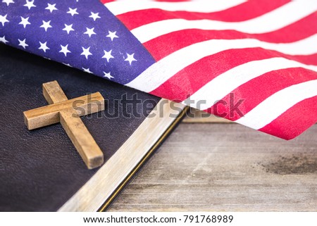 An American flag with a wooden Christian cross and a holy Bible on a wood background.