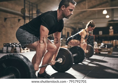 Sporty man and woman are about to lift barbells in gym. Horizontal indoors shot Royalty-Free Stock Photo #791792701