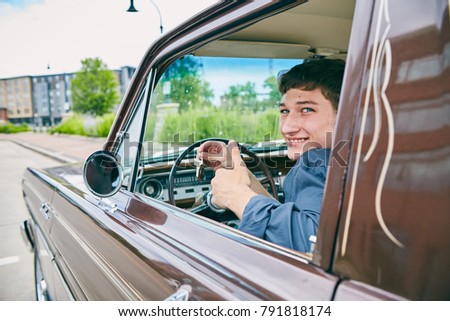 Face of happy male driver sitting in car, showing keys in car window, looking at camera and smiling